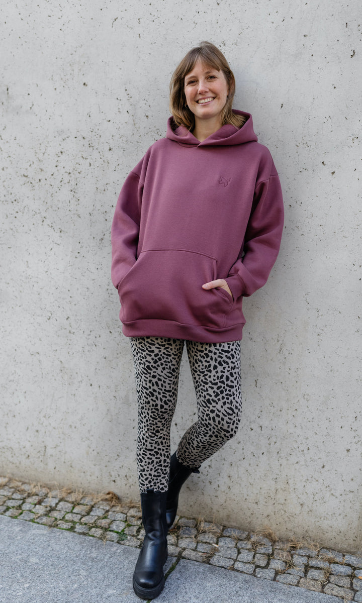 Stillhoodie in feige rosa vor grauer Wand kombiniert mit Leo Leggings und schwarzen Stiefeln von vorne Blick gerade lächelnd