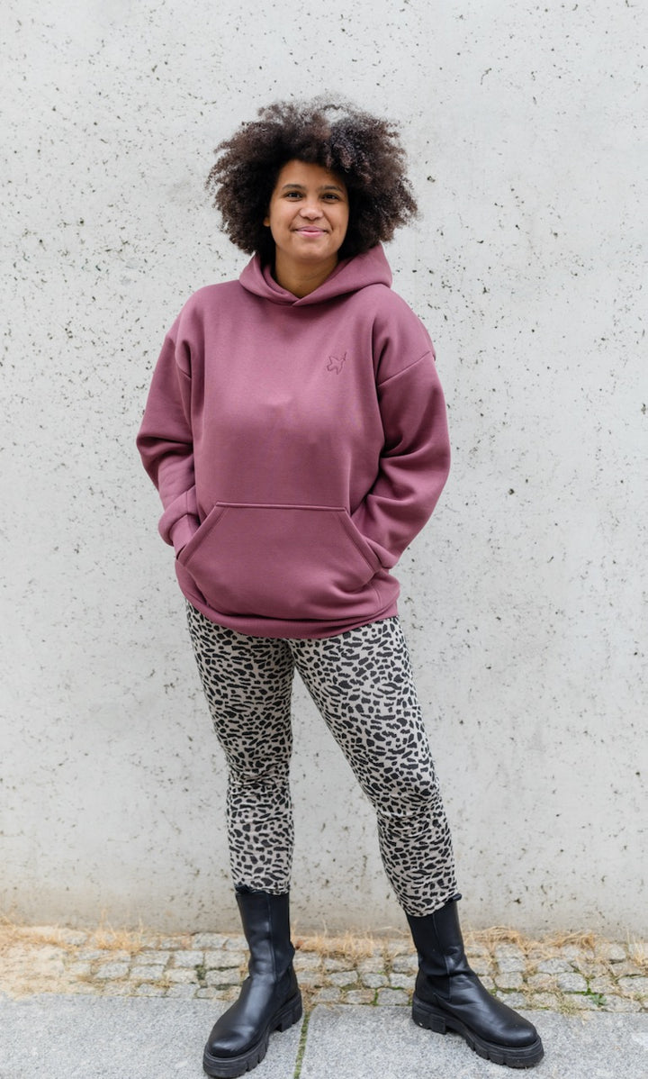 Stillhoodie in feige rosa vor grauer Wand kombiniert mit Leo Leggings und schwarzen Stiefeln von vorne Blick gerade