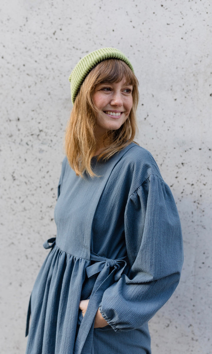 Stillkleid Anouk im Herbst in karo blau mit Mütze Hände in Taschen vor Wand