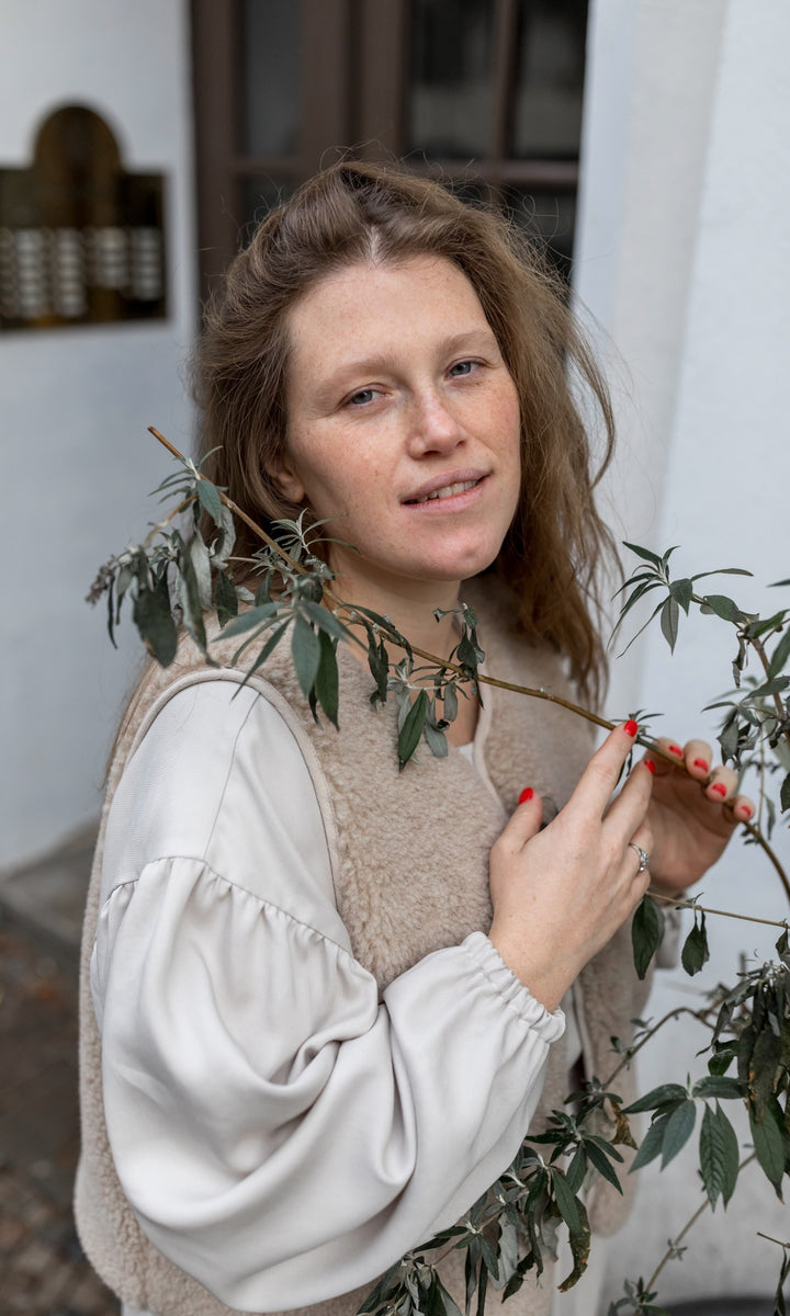 Stillkleid Shania in creme weiß mit Schafwoll-Weste seitlich hinter Baum