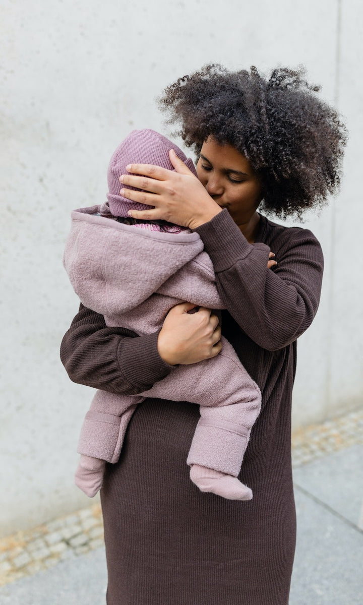 Stillkleid Jules in braunem Strick frontale Ansicht mit Baby auf Arm vor Wand stehend
