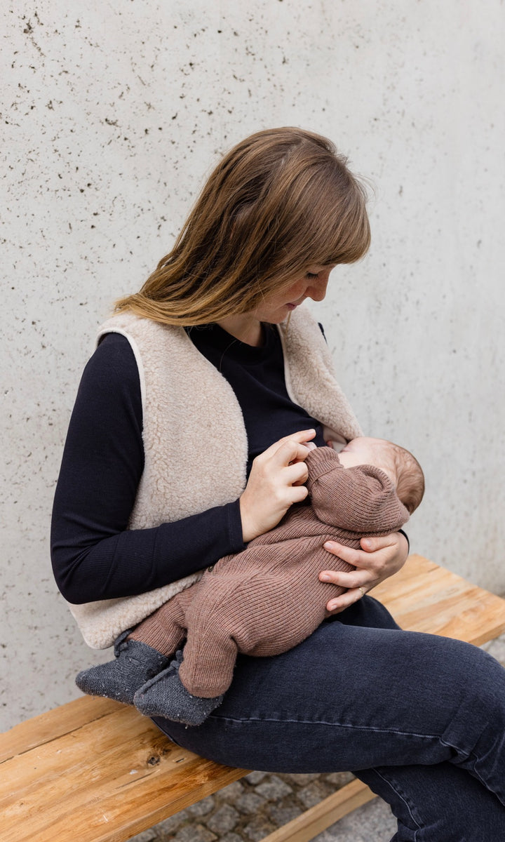 Longsleeve Stilloberteil Cléo mit Rollkragen in schwarz kombiniert mit heller Schafwoll-Weste beim Stillen mit Stillfunktion im Winter Blick zu Baby