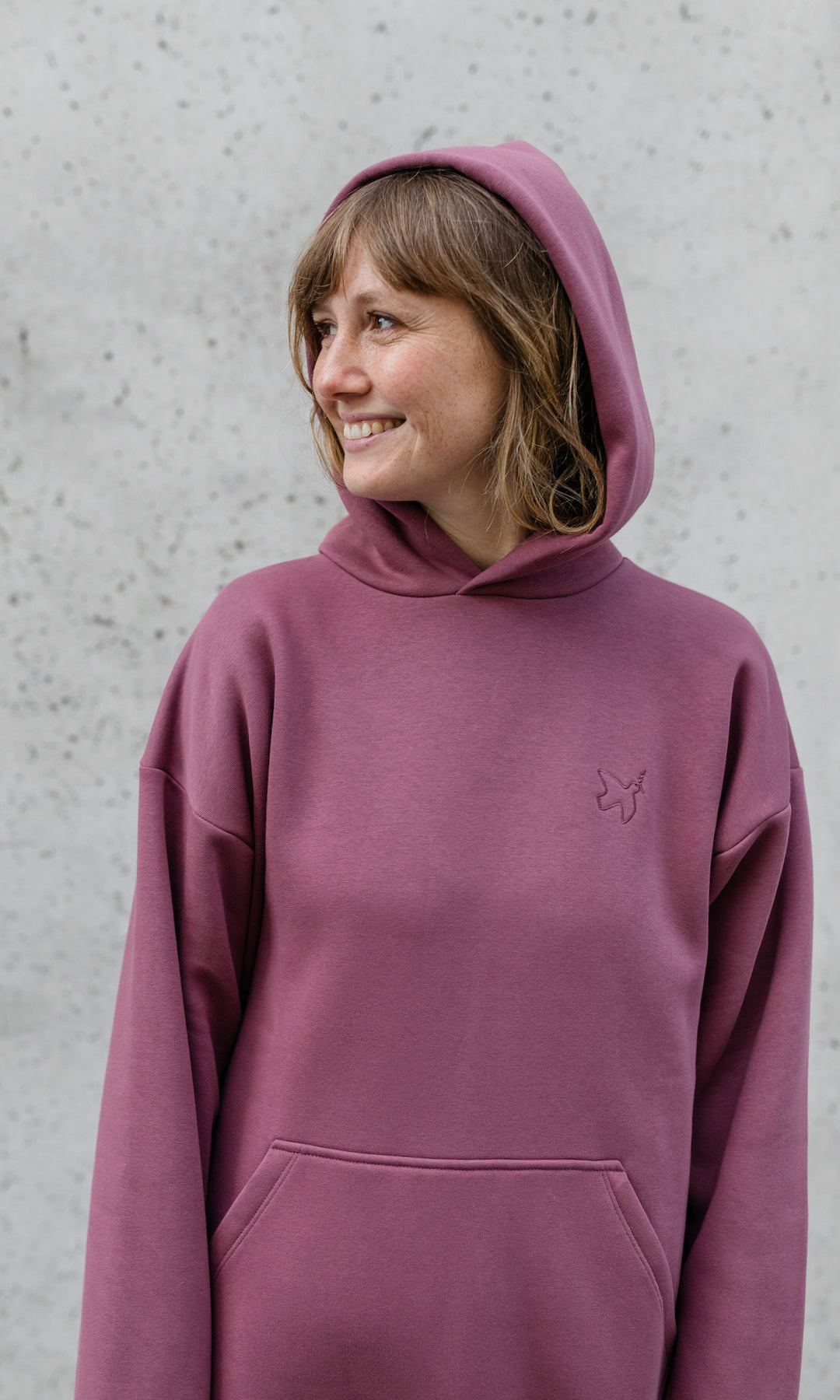 Stillpullover in feige rosa mit Kapuze auf Kopf lächelnd von vorne Blick seitlich