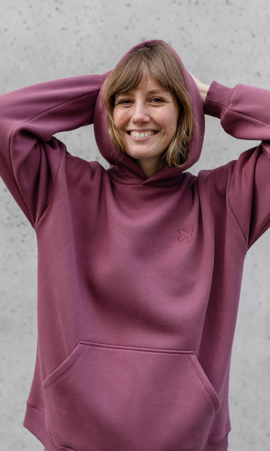 Stillpullover in feige rosa mit Kapuze auf Kopf lachend von vorne