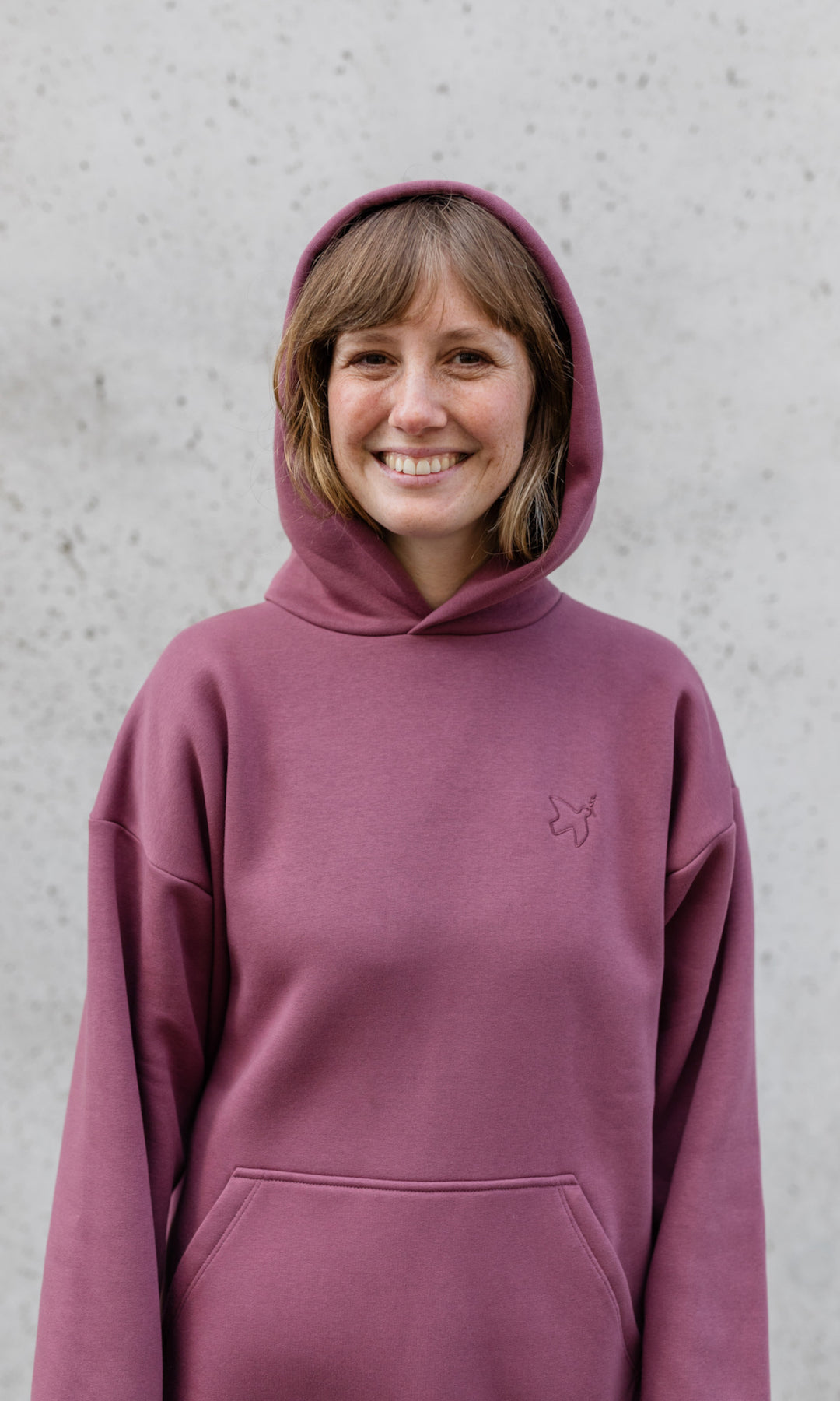 Stillpullover in feige rosa mit Kapuze auf Kopf lächelnd von vorne