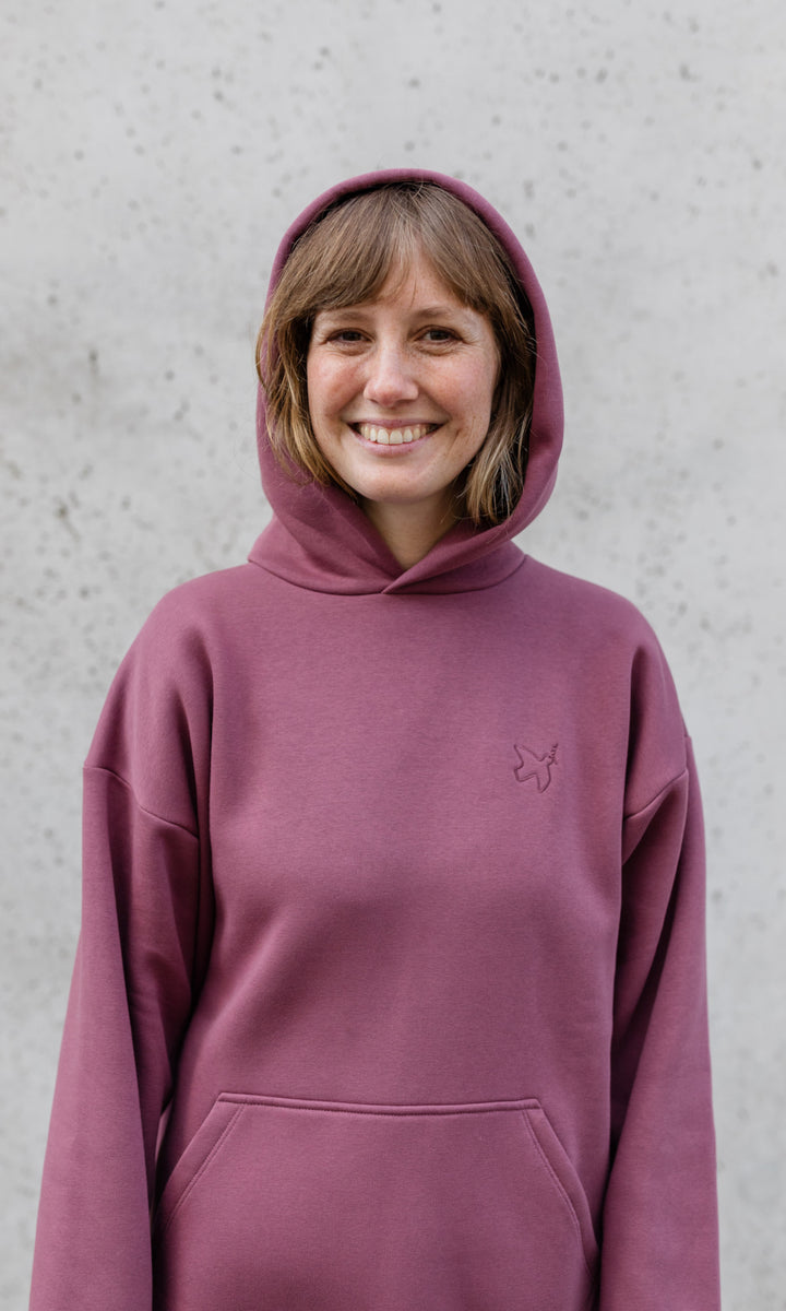 Stillpullover in feige rosa mit Kapuze auf Kopf lächelnd von vorne