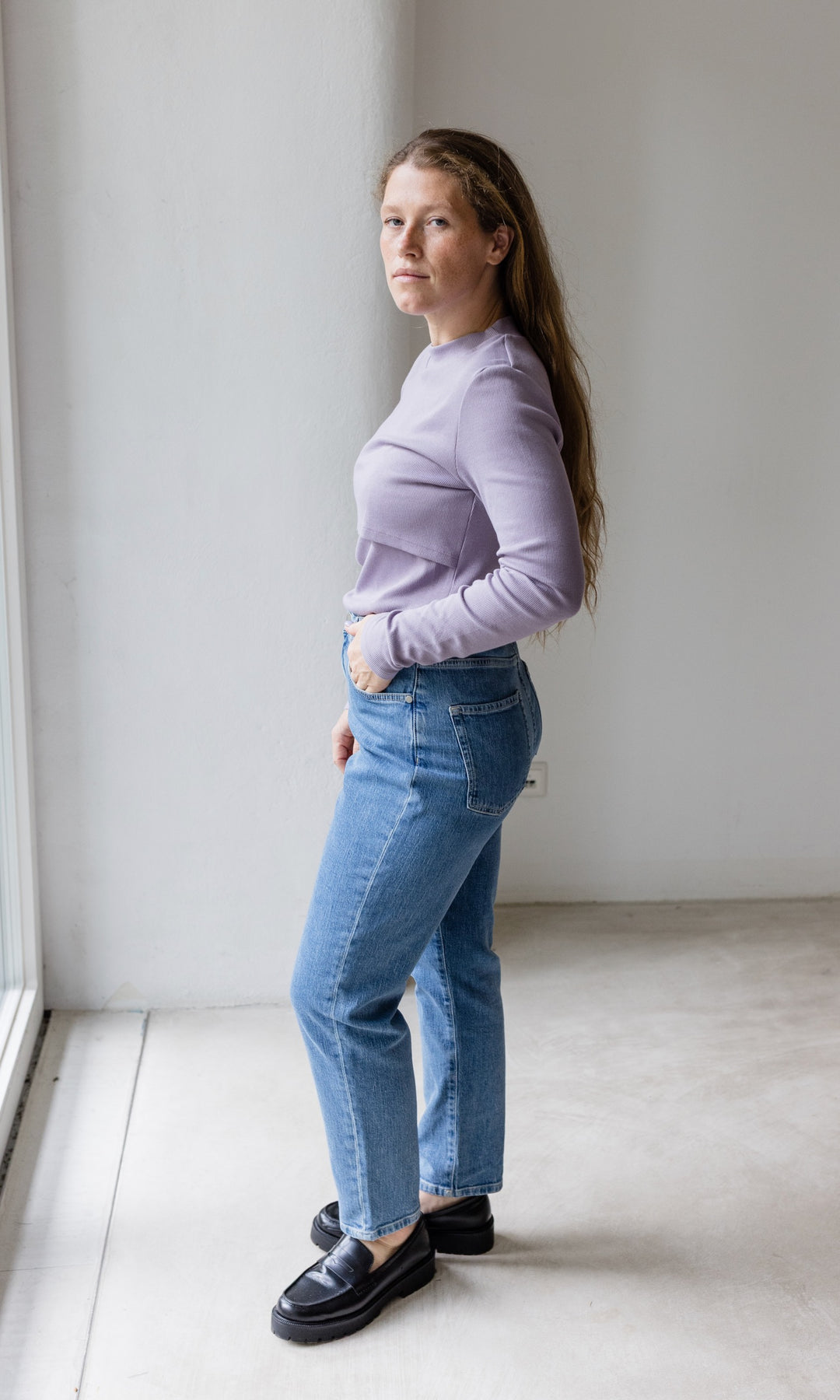 Stillshirt lang mit Rollkragen in flieder kombiniert mit hellblauer Jeans vor grauer Wand seitlich Blick seitlich