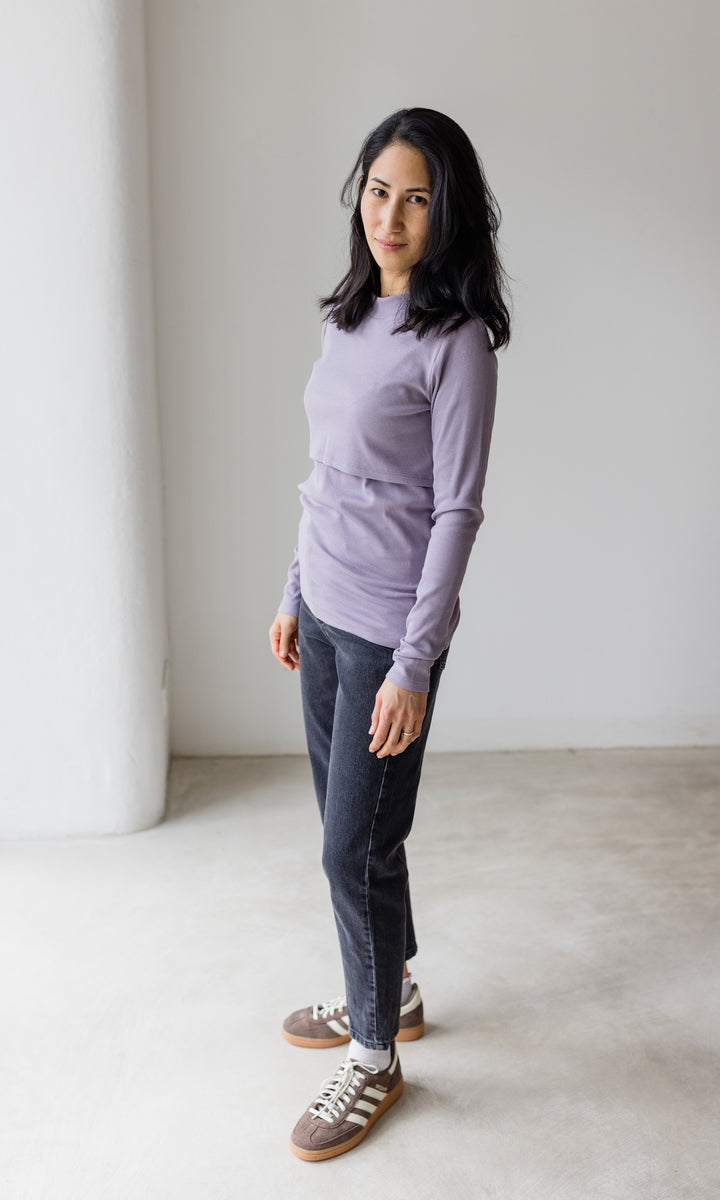Stillshirt lang mit Rollkragen in flieder kombiniert mit dunkelblauer Jeans und Sneakers vor grauer Wand seitlich Blick seitlich