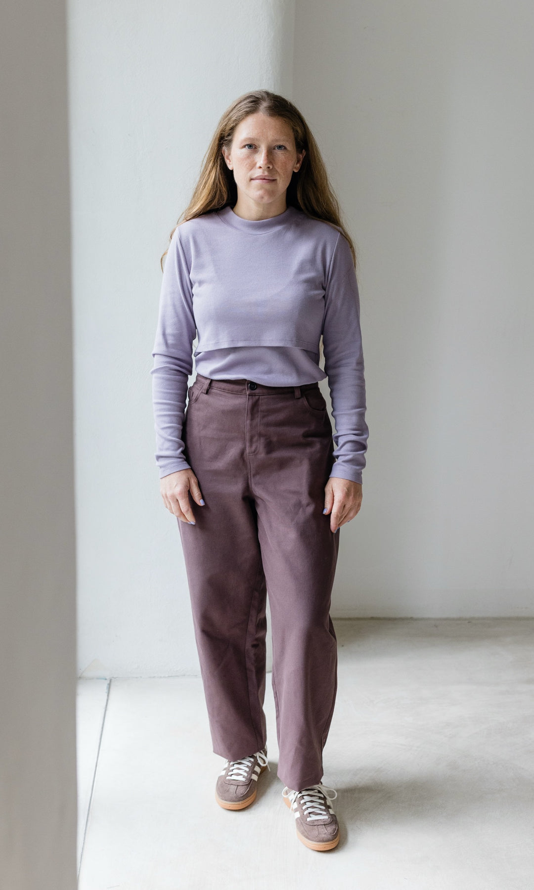 Stillshirt lang mit Rollkragen in flieder kombiniert mit roter, lila Hose und Sneakers vor grauer Wand von vorne Blick gerade