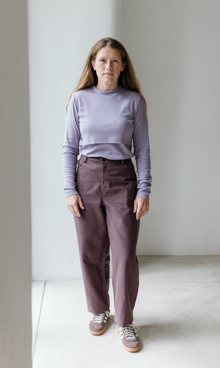 Stillshirt lang mit Rollkragen in flieder kombiniert mit roter, lila Hose und Sneakers vor grauer Wand von vorne Blick gerade