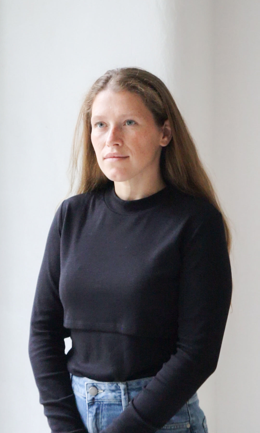 Langarm Stillshirt Cléo mit Rollkragen in schwarz kombiniert mit hellblauer Jeans vor grauer Wand seitlich Blick gerade lächelnd