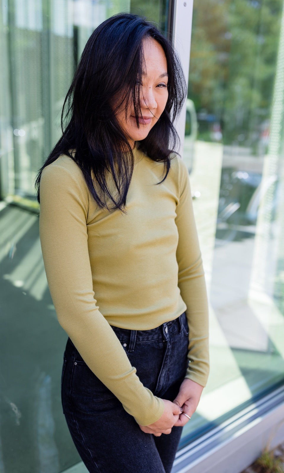 Stillshirt langarm Cléo mit Rollkragen in olive grün kombiniert mit dunkelblauer Jeans vor Fensterscheibe seitlich Blick gerade