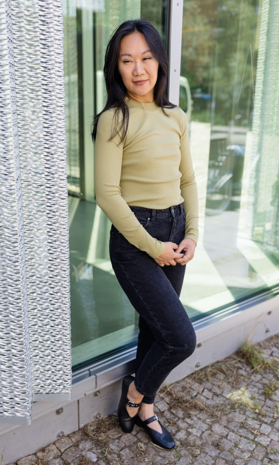 Stillshirt langarm Cléo mit Rollkragen in olive grün kombiniert mit dunkelblauer Jeans vor Fensterscheibe seitlich Blick seitlich