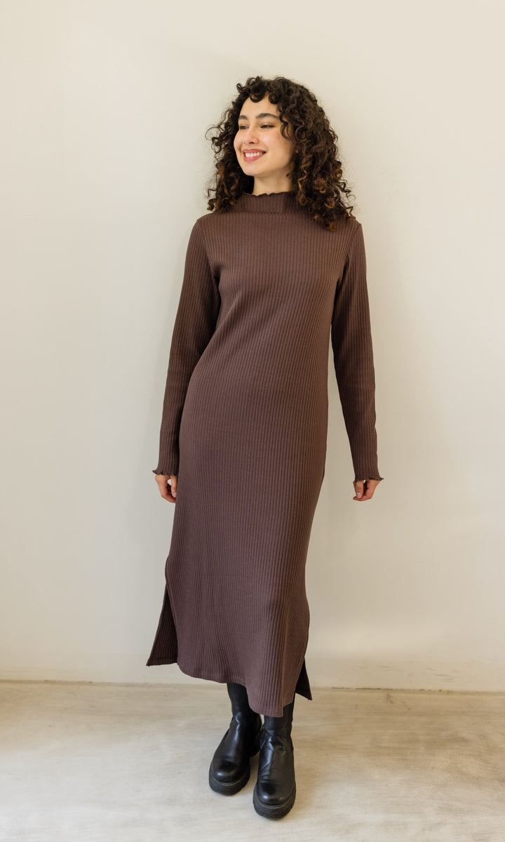 Strickkleid Jil aus Baumwolle in braun langarm mit schwarzen Stiefeln vor heller Wand Blick seitlich lachend