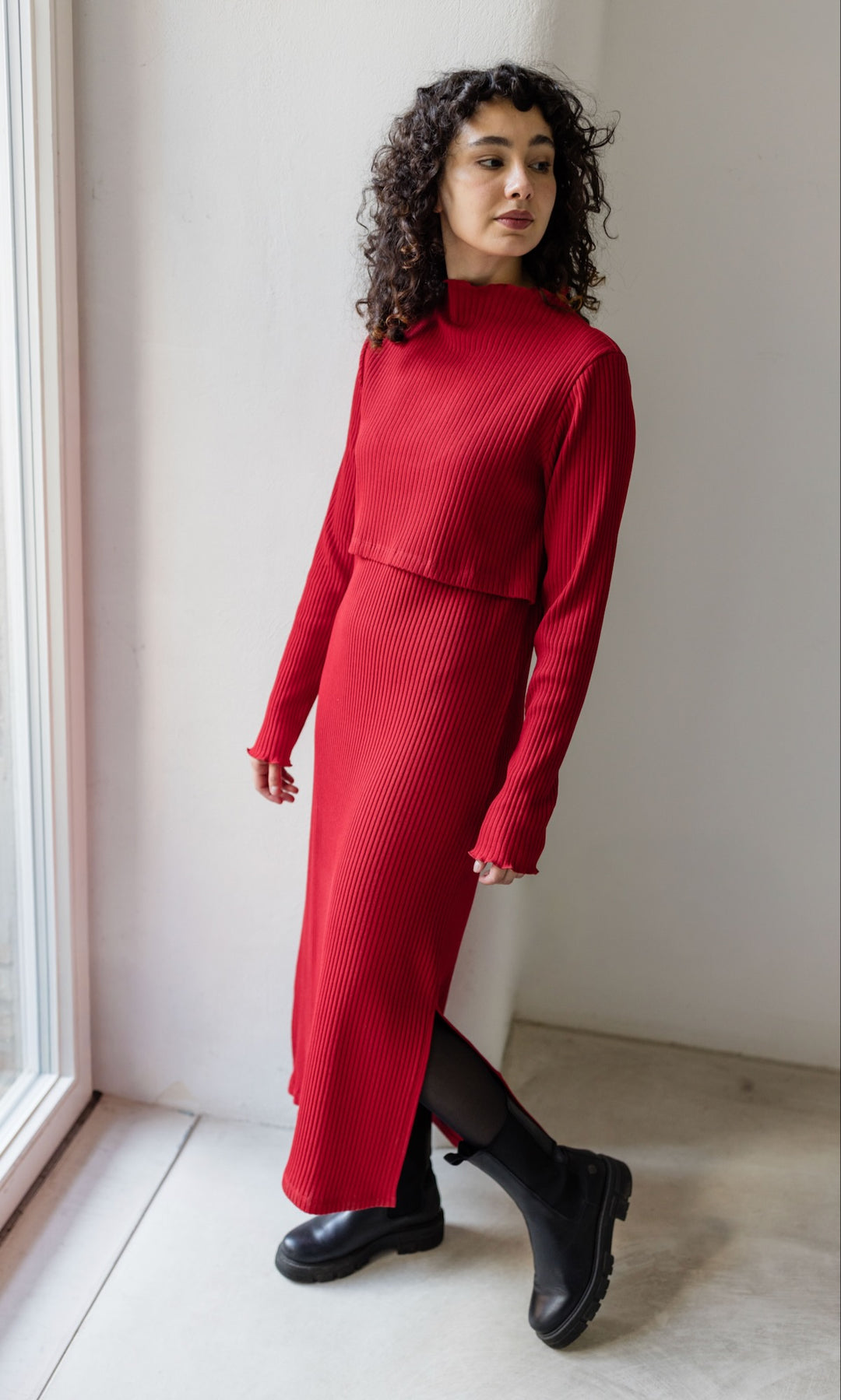 Strickkleid Jil rot lang in langarm mit Stillfunktion Outfit mit schwarzen Stiefeln seitlich stehend vor heller Wand Blick seitlich