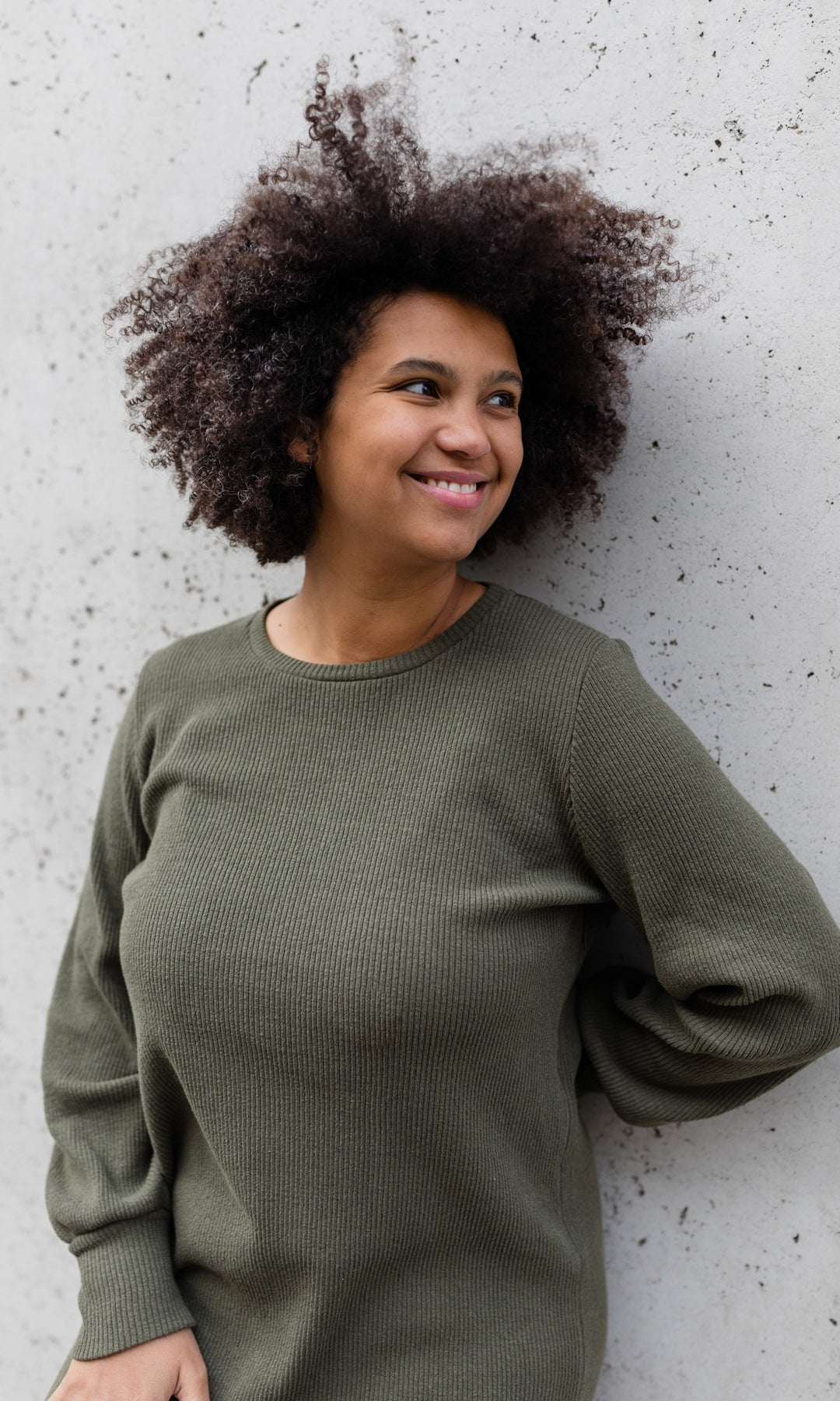 Strickkleid Jules in grün olive an heller Wand gelehnt