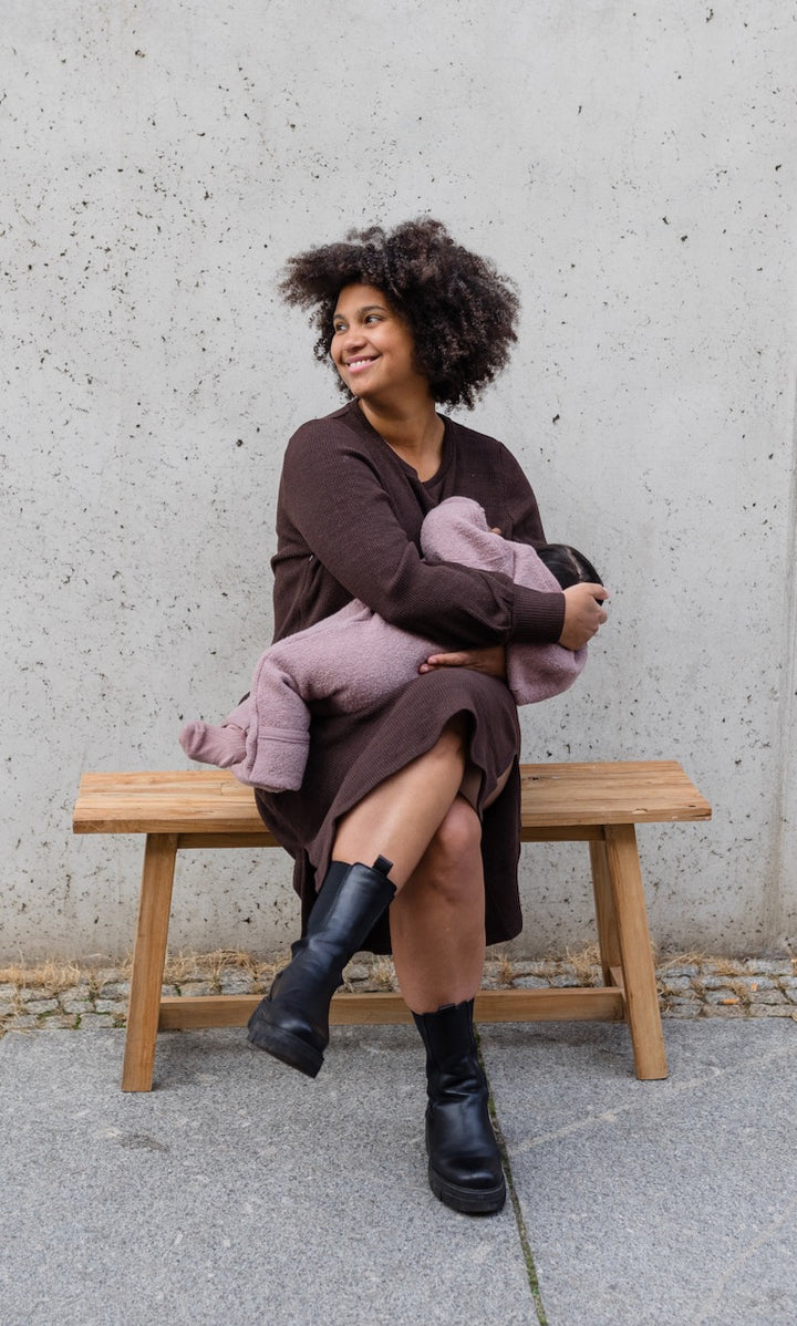 Strickkleid Jules in braun mit seitlicher Stillfunktion sitzend auf Bank vor Wand mit Baby beim Stillen