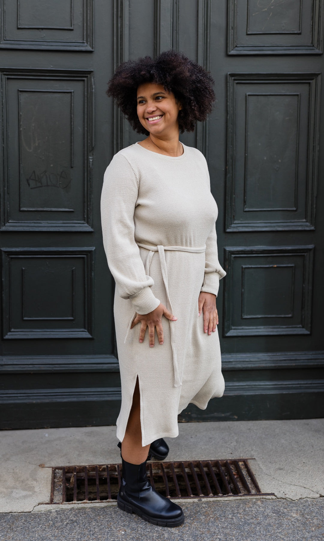 Strickkleid Jules mit seitlicher Stillfunktion in creme beige vor Tür seitlicher Blick