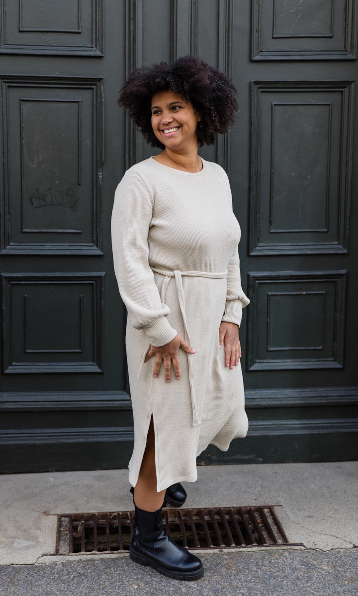 Strickkleid Jules mit seitlicher Stillfunktion in creme beige vor Tür seitlicher Blick