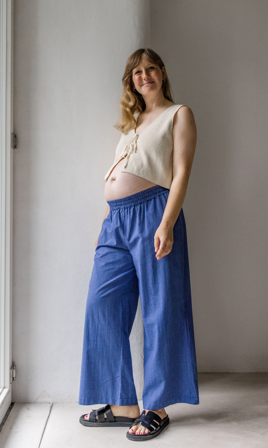 Seitenansicht Umstandshose Ivy Culotte in blau kombiniert mit hellem Baumwoll-Strickpullunder und schwarzen Sandalen.