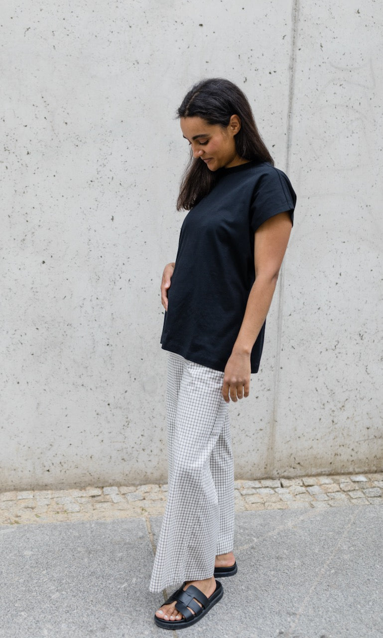 Umstandshose Ivy Culotte in karo weiß kombiniert mit dunkelblauem T-Shirt und schwarzen Sandalen. Außenaufnahme vor heller Hauswand.