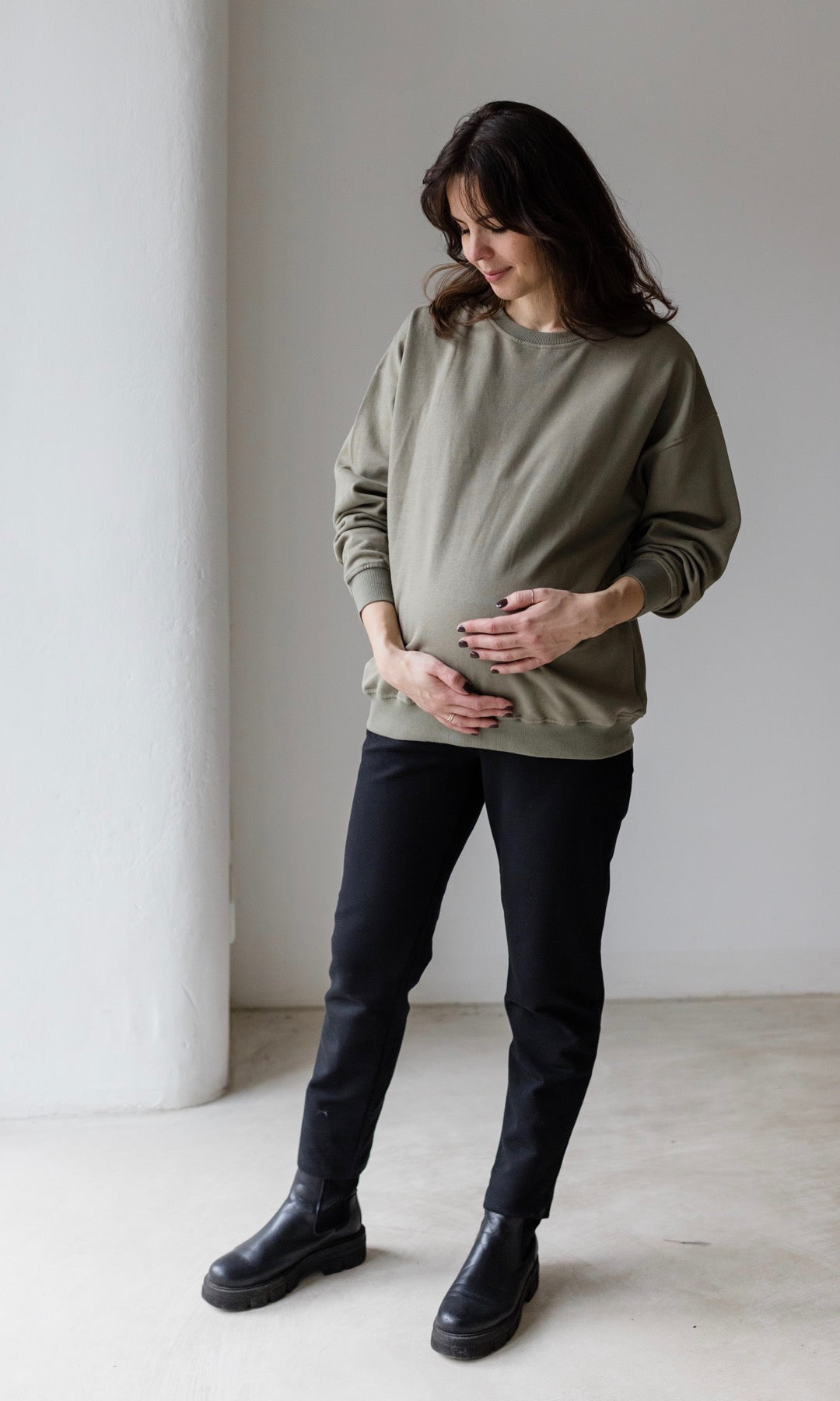 Umstandshose Mom in schwarz kombiniert mit oliv grünem oversized Pullover und schwarzen Schuhen.
