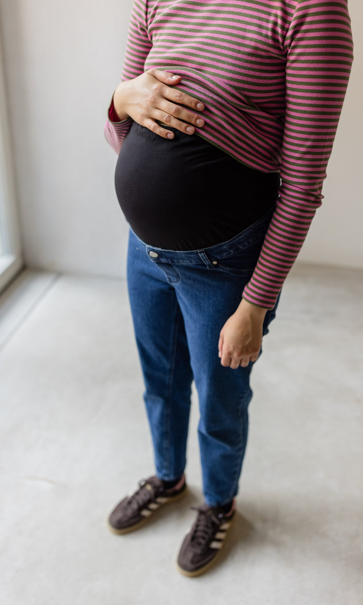 Umstandsjeans in dunkelblau im Mom Fit Look kombiniert mit gestreiftem Langarmshirt und braunen Sneakers Detail Babybauch mit elastischem Bauchbund