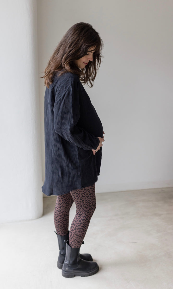 Umstandsleggings braun leo Print mit schwarzem Musselin Hemd schwarzen Stiefeln seitlich vor heller Wand Blick nach unten