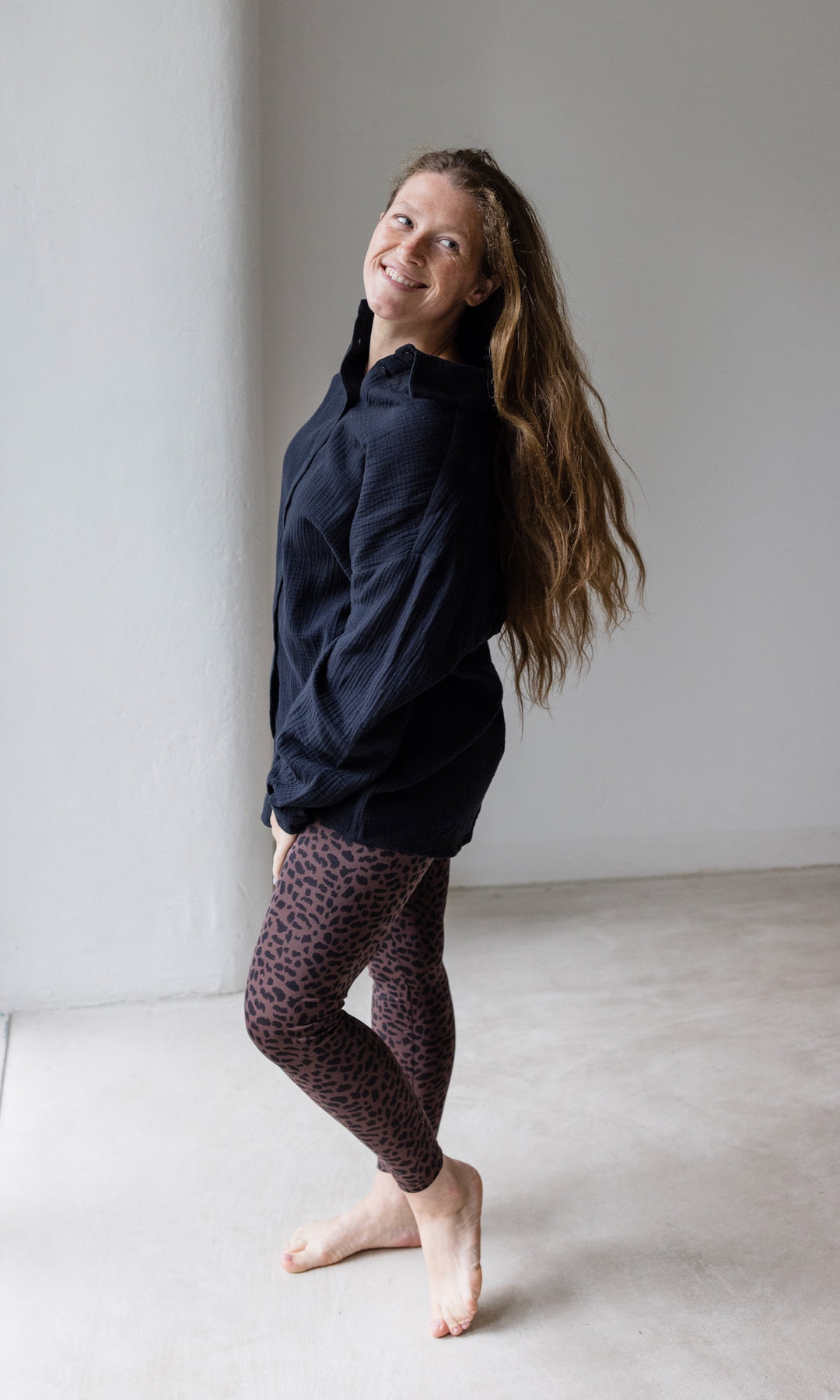 Umstandsleggings braun leo Print mit schwarzem Musselin Hemd seitlich vor heller Wand Blick nach vorne lachend