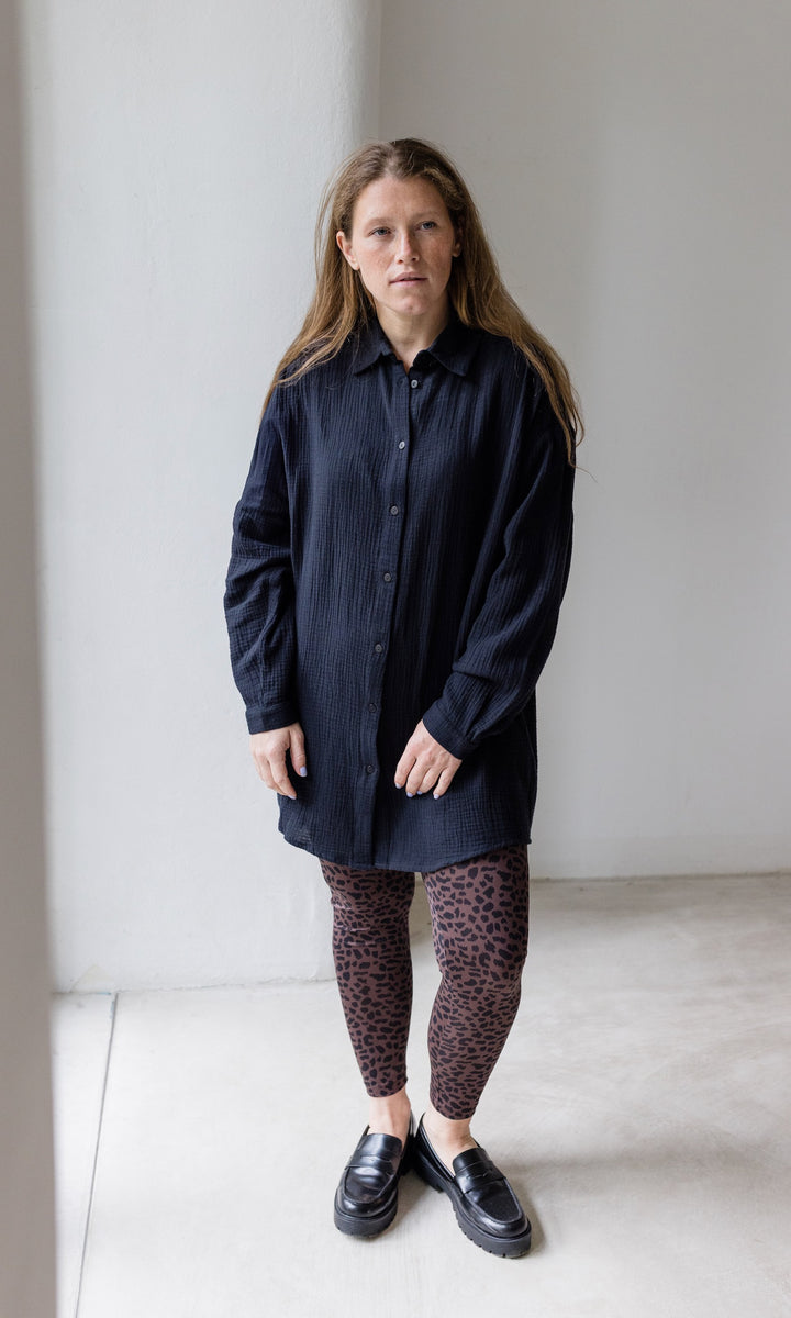 Umstandsleggings braun leo Print mit schwarzem Musselin Hemd schwarzen Schuhen vor heller Wand Blick nach vorne