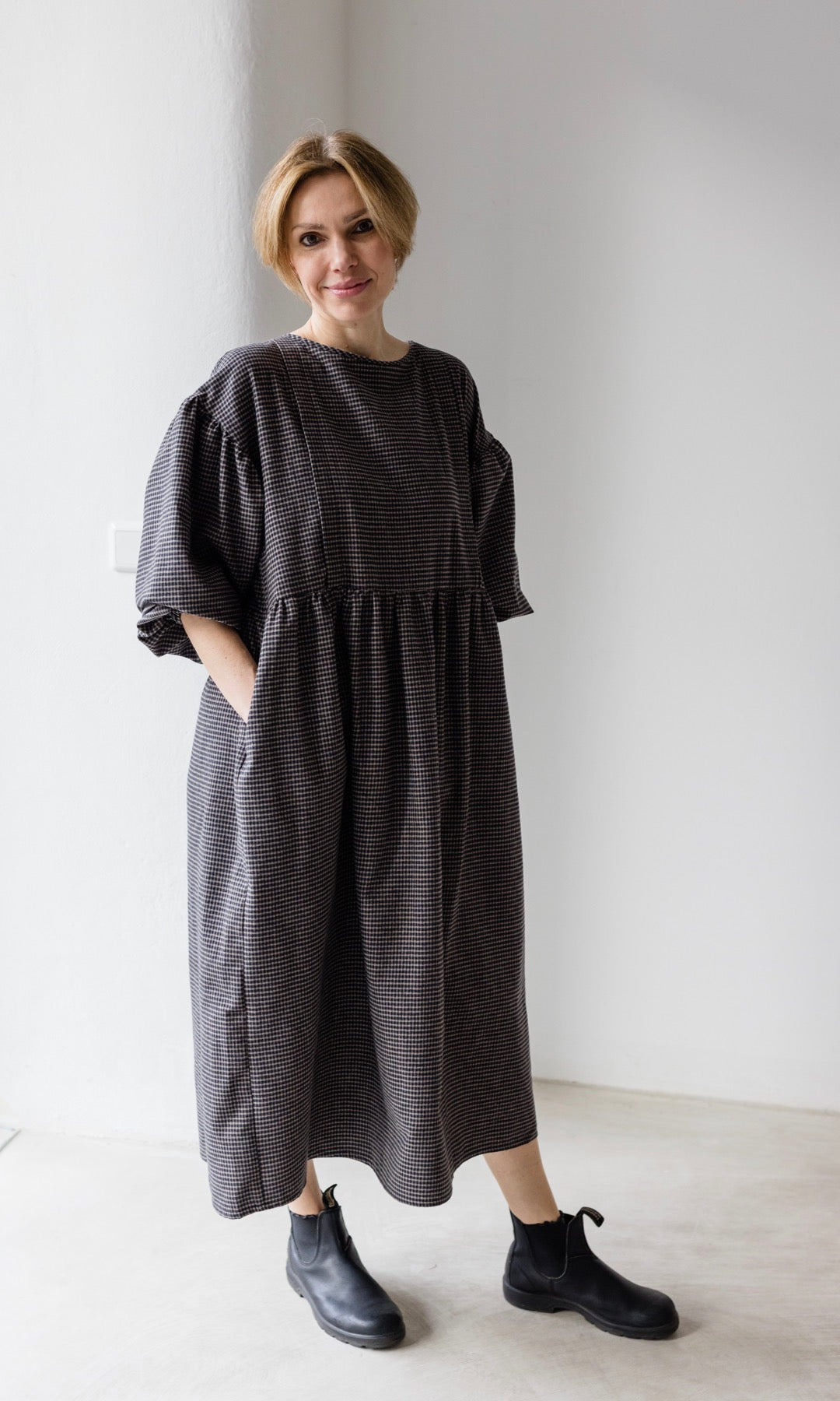 Winter Stillkleid Lovis in karo schwarz mit schwarzen Boots Blick nach vorne Hände in Taschen
