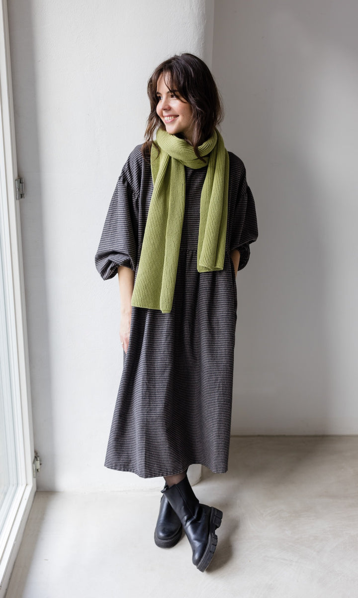 Winter Stillkleid Lovis in karo schwarz mit schwarzen Stiefeln und grünem Schal seitlich Blick seitlich lächelnd