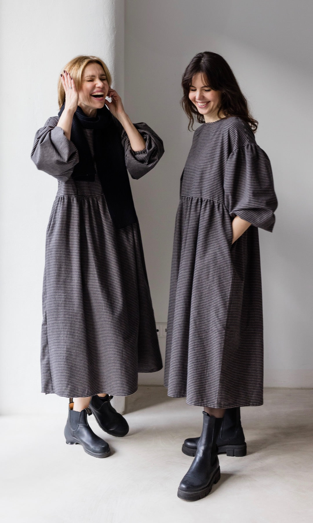 Winter Stillkleid Lovis in karo schwarz in zwei Looks mit schwarzen Stiefeln eine Variante mit schwarzem Schal Hände in Taschen lachend