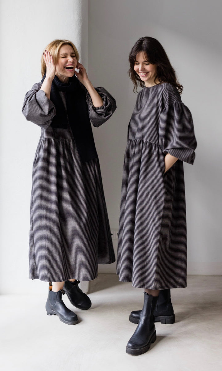 Winter Stillkleid Lovis in karo schwarz in zwei Looks mit schwarzen Stiefeln eine Variante mit schwarzem Schal Hände in Taschen lachend