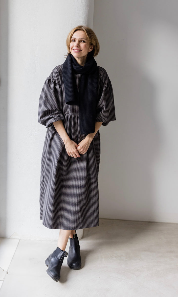 Winter Stillkleid Lovis in karo schwarz mit schwarzen Stiefeln und schwarzem Schal frontal lächelnd