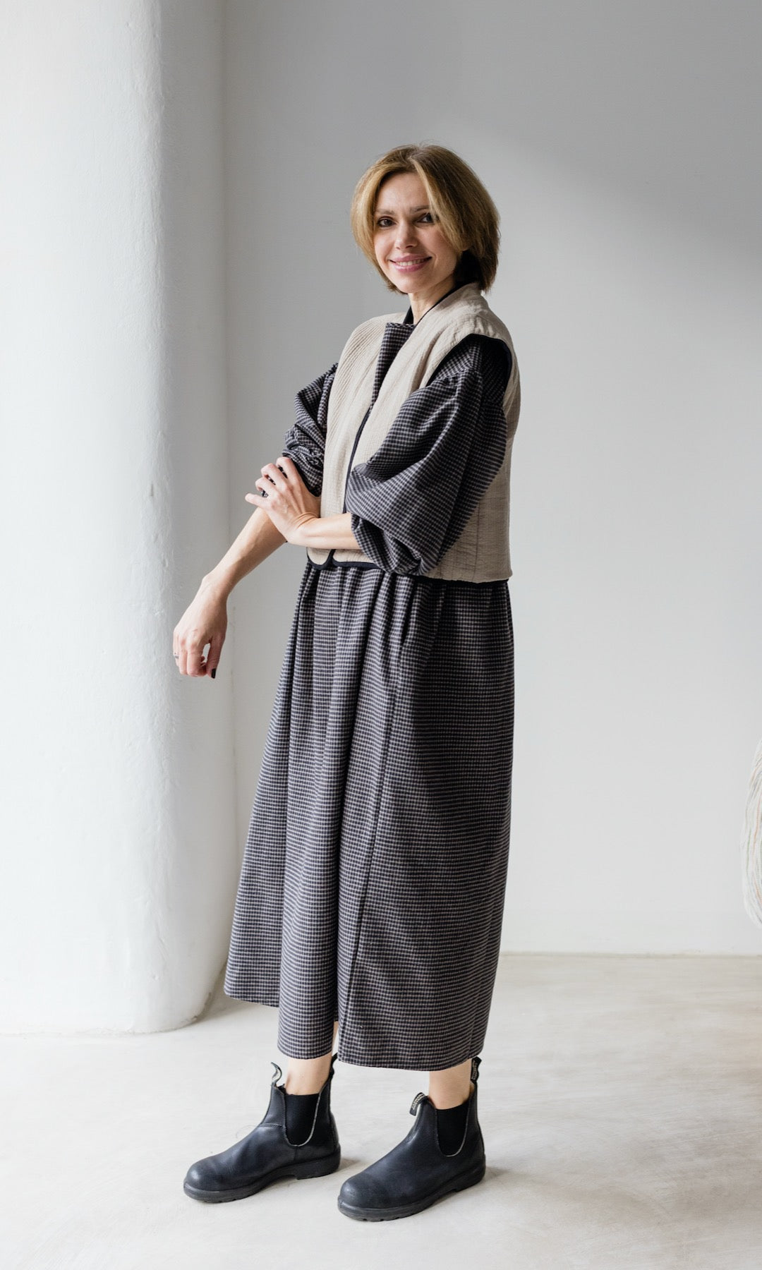 Winter Stillkleid Lovis in karo schwarz mit schwarzen Stiefeln und heller Weste seitliche Ansicht lächelnd