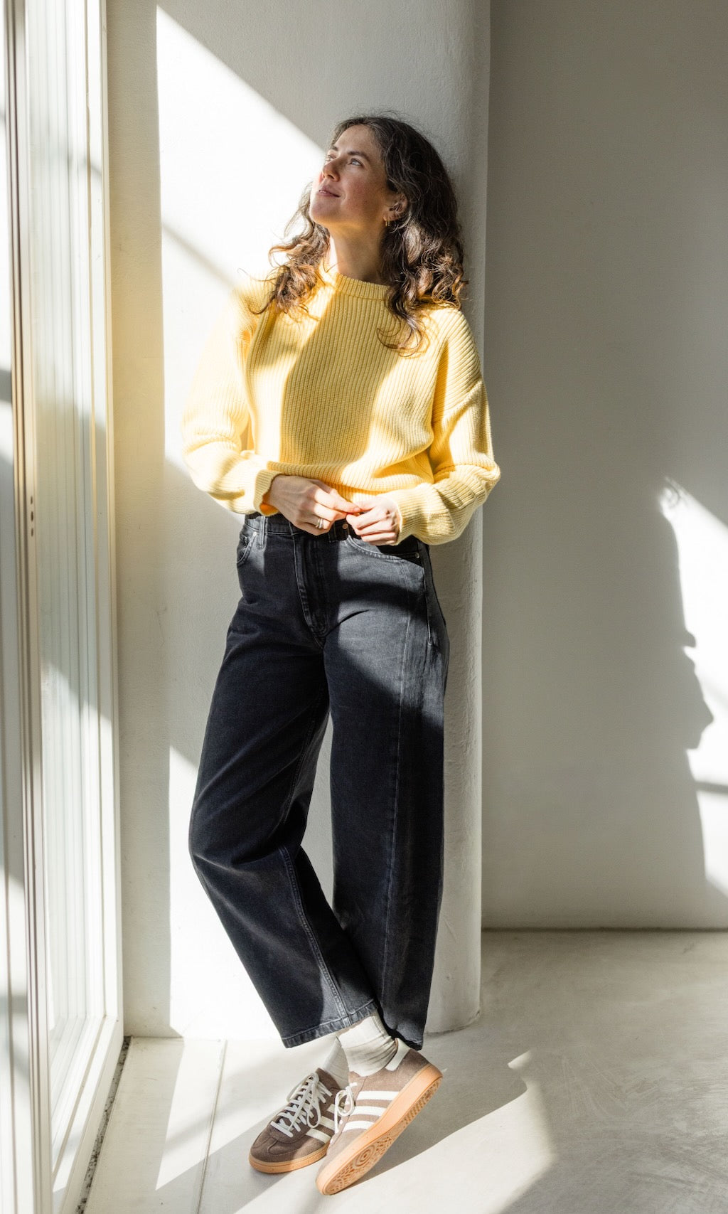 Zitronengelber Strickpullover aus Bio-Baumwolle kombiniert mit schwarzer Barrel-Jeans und braunen Sneakers für ein lässiges Freizeit-Outfit.