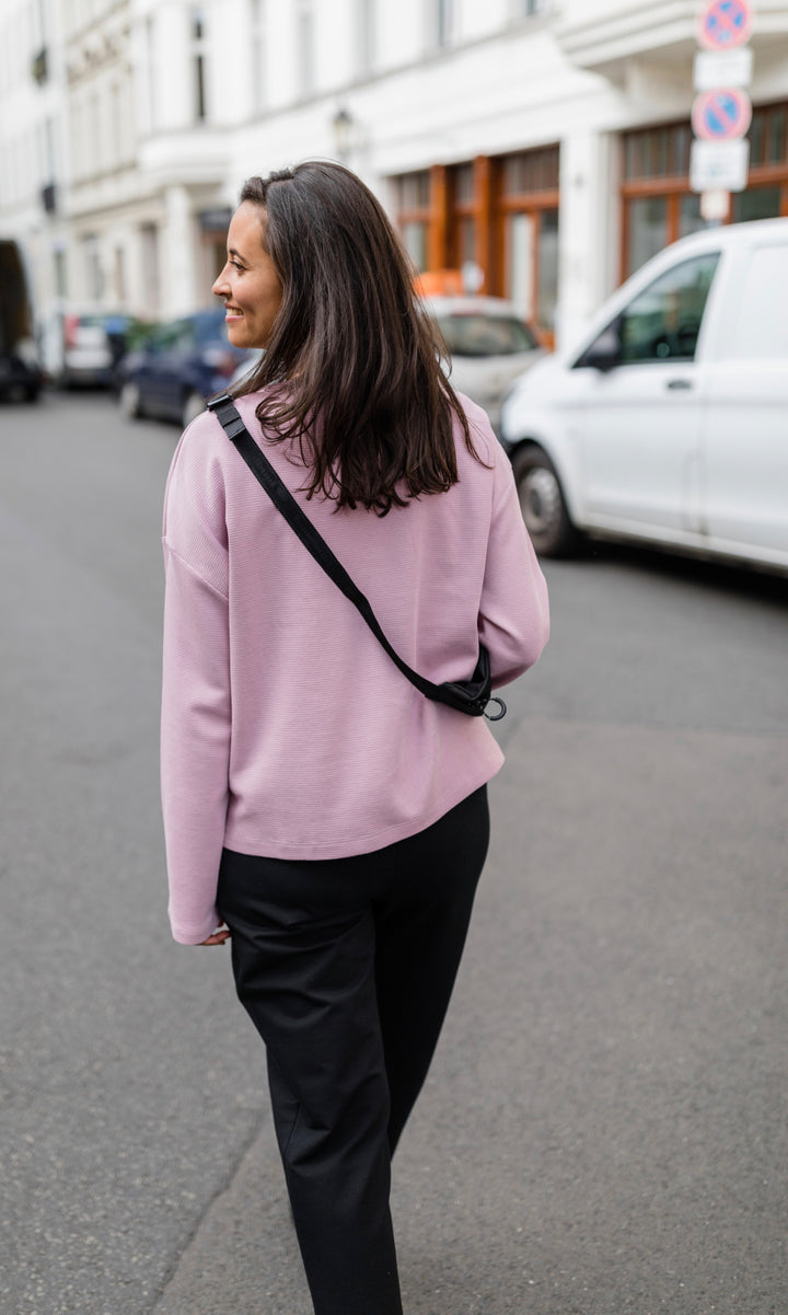 Rückansicht Umstandshose in schwarz im Look mit pinkem Langarmshirt und schwarzer Handtasche. Außenaufnahme in Berliner Straße.