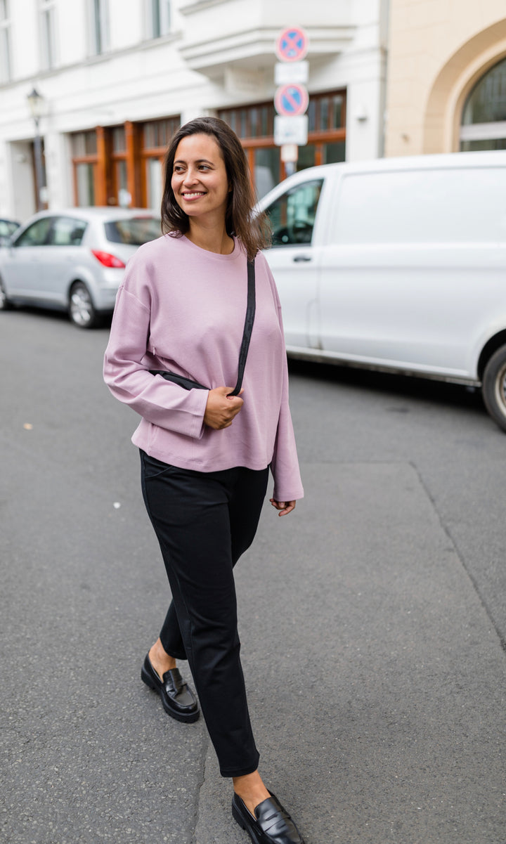 Schwarze Umstandshose im Look mit pinkem Langarmshirt und schwarzer Handtasche. Außenaufnahme in Berliner Straße.