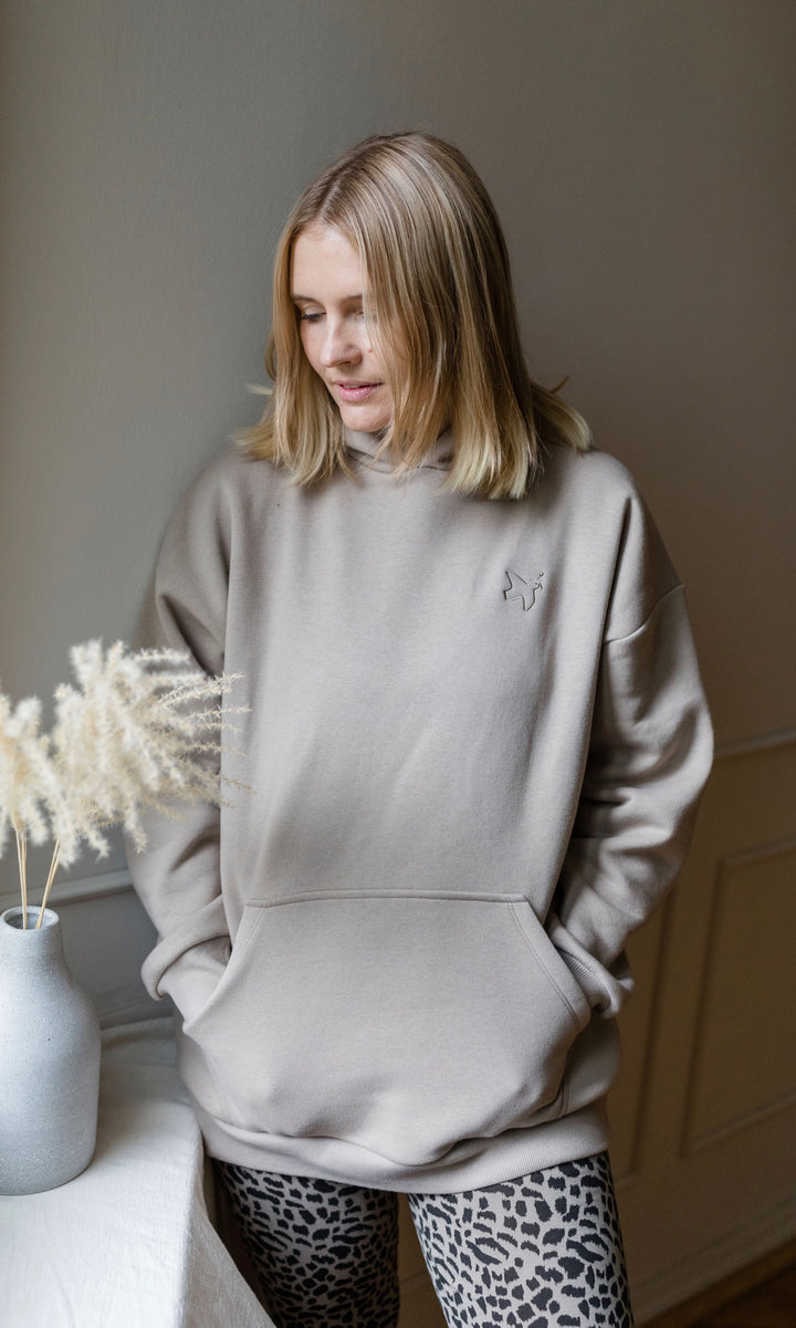 Stillhoodie in sesam weiß stehend mit Leo Leggings neben Tisch Hände in Tasche 