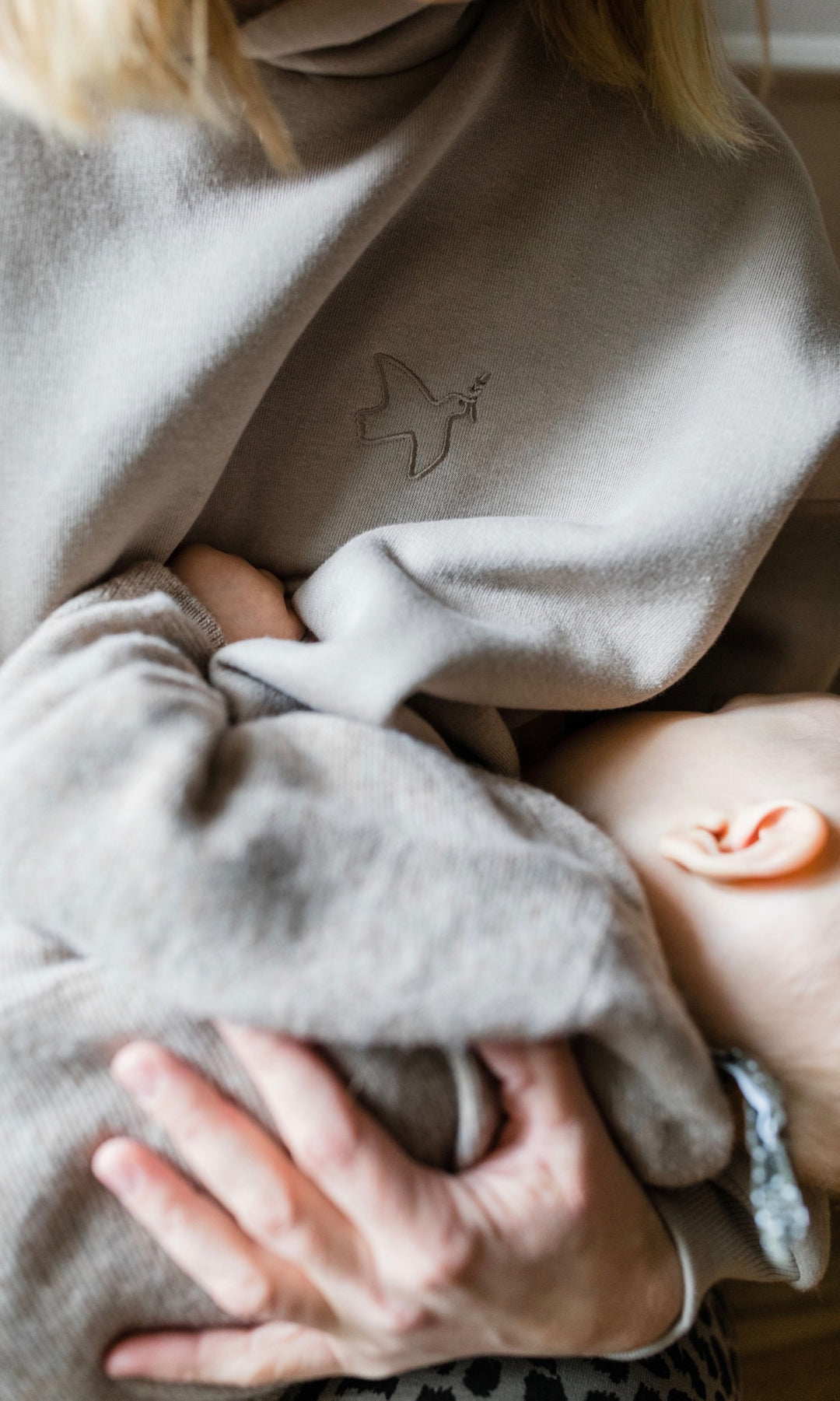 Stillhoodie in sesam weiß sitzend mit Baby auf Arm beim Stillen mit geöffnetem Reißverschluss