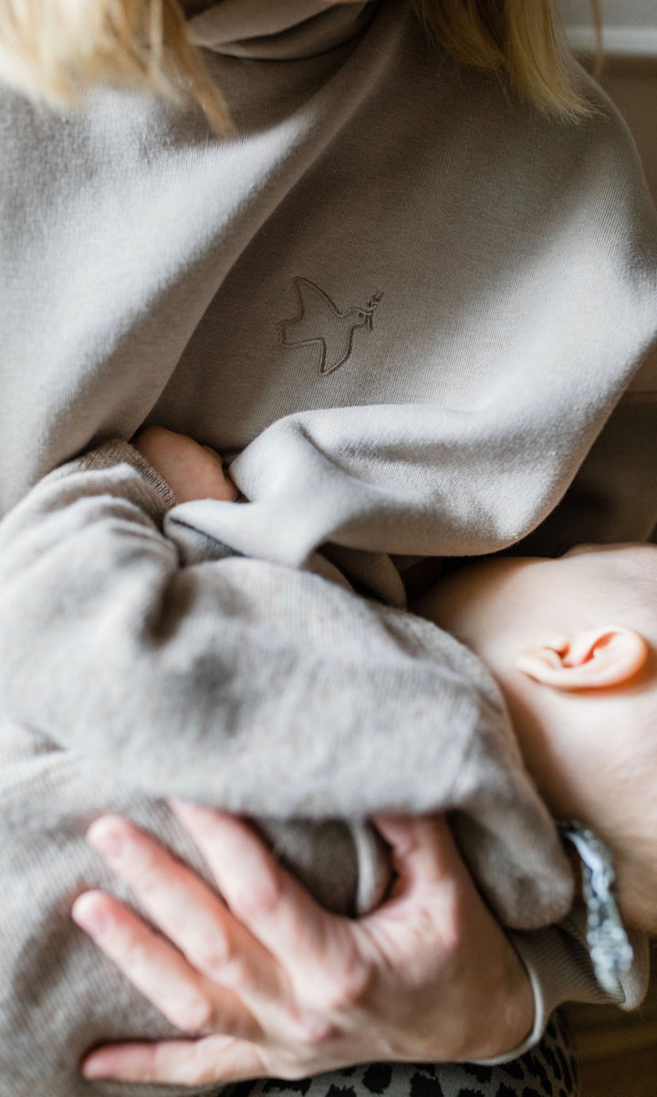 Stillhoodie in sesam weiß sitzend mit Baby auf Arm beim Stillen mit geöffnetem Reißverschluss