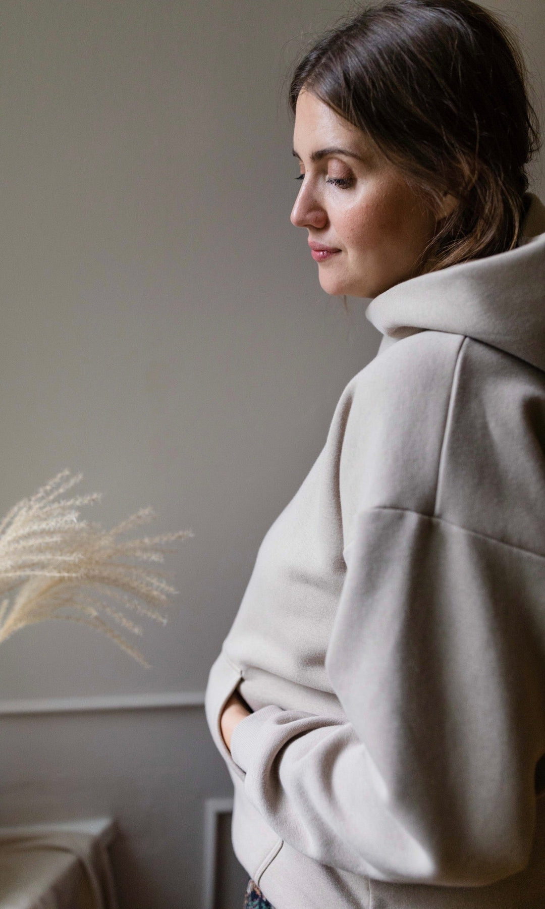 Stillhoodie in sesam weiß seitlich stehend neben Tisch Hand in Tasche seitlich Blick nach vorne