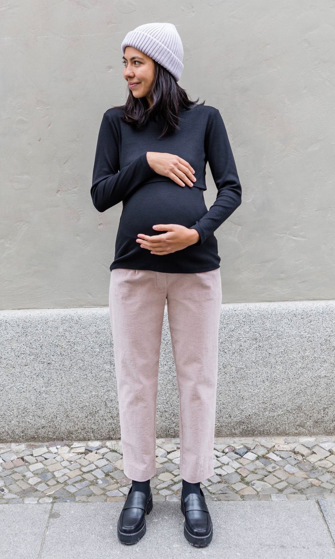 Langarm Stilloberteil Cléo mit Rollkragen in schwarz kombiniert mit heller Hose und Wollmütze und schwarzen Schuhen vor grauer Wand im Winter von vorne Blick seitlich