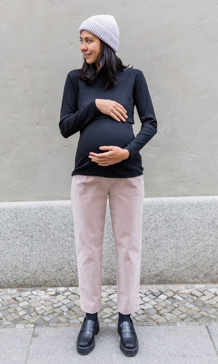 Langarm Stilloberteil Cléo mit Rollkragen in schwarz kombiniert mit heller Hose und Wollmütze und schwarzen Schuhen vor grauer Wand im Winter von vorne Blick seitlich