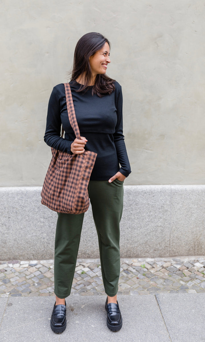 Langarm Stillshirt Cléo mit Rollkragen in schwarz kombiniert mit grüner Hose, karierter Tasche und schwarzen Schuhen vor grauer Wand im Herbst von vorne Blick seitlich lachend